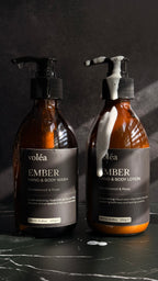 Two amber pump bottles of voléa hand and body wash and hand and body lotion on a dark marble surface against a dark textured background.