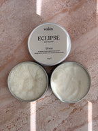Volea Eclipse Shea Body Butter in a round silver tin, with one tin open to show the creamy off-white balm inside and another tin showing its lid label.