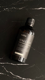 A bottle of Volea Halcyon Body & Bath Rituals resting on a dark marble surface with white veining.